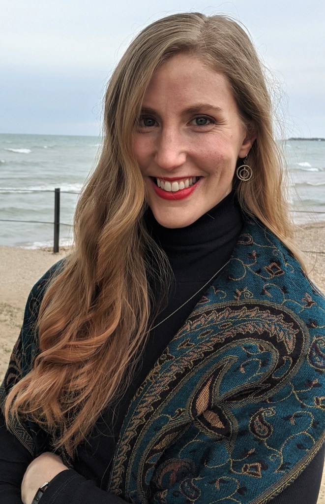 photo showing Lauren smiling and wearing a black turtleneck and green patterned scarf standing in front of Lake Michigan.